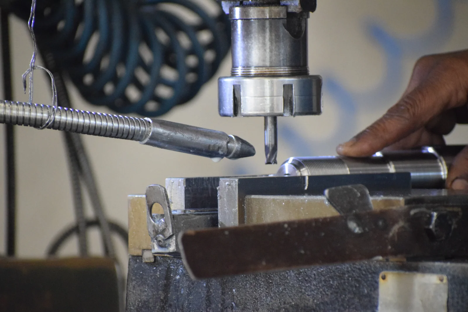 Drilling a metal component held in a vice, with a spiral screw flight in the background