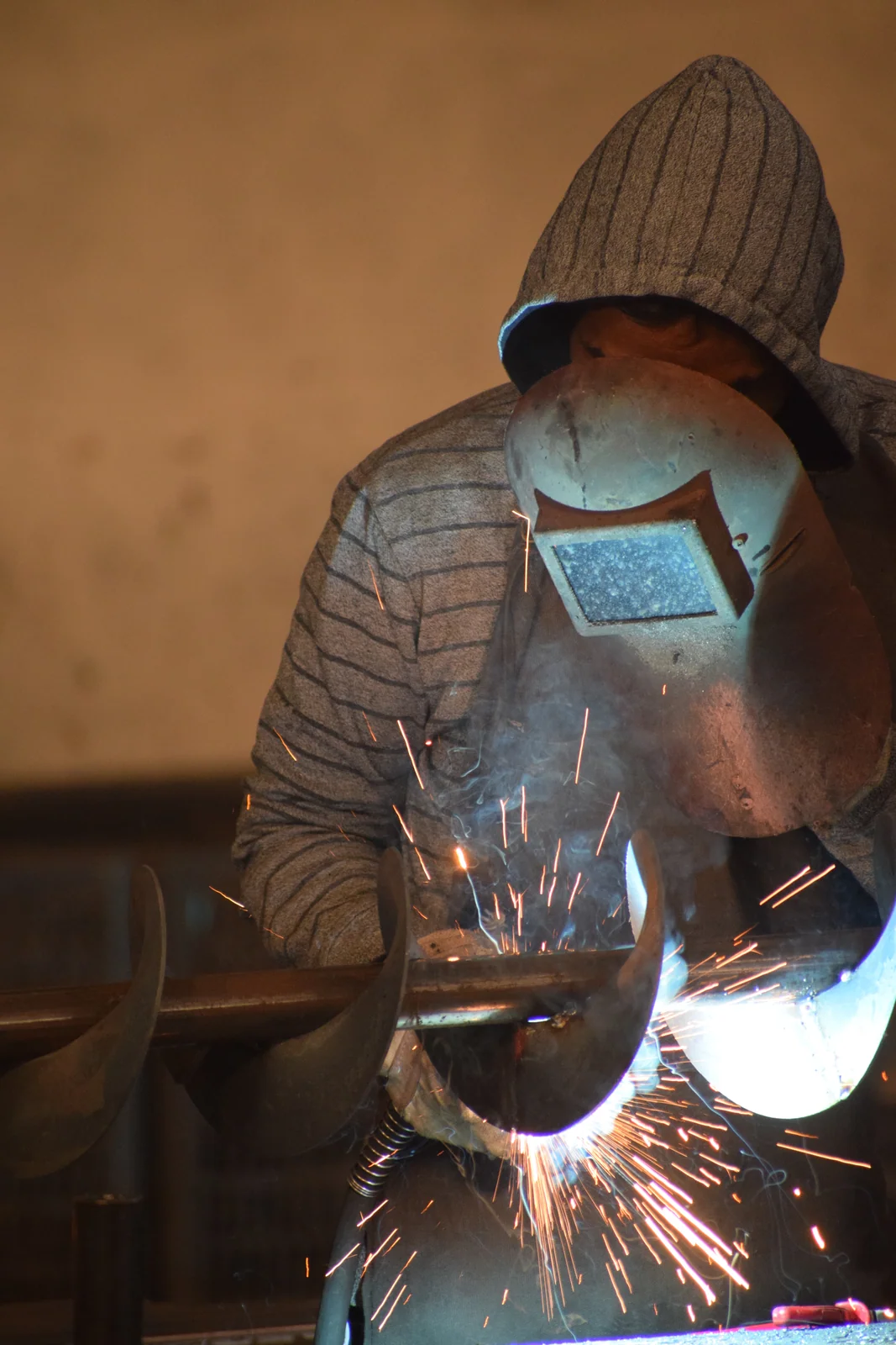 Welder in a protective mask welding a steel component with bright sparks