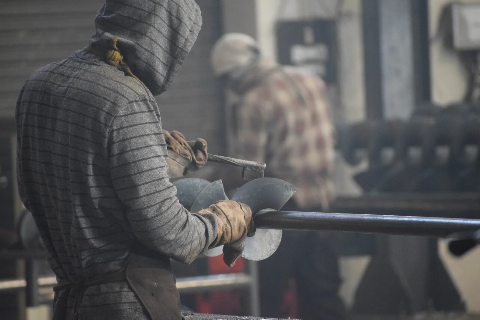 Worker grinding and finishing a steel shaft in the workshop
