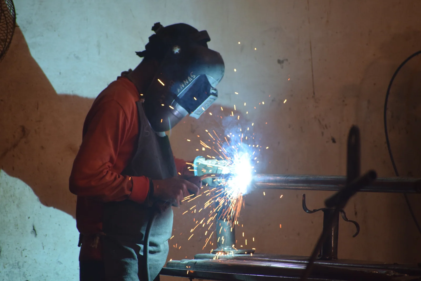 Welder in a helmet arc-welding a fabricated steel part