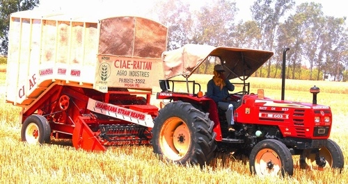 Tractor-driven Jhandeana straw reaper with trolley working in a wheat field